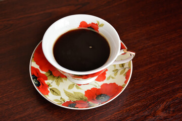 Poppy cup of coffee with the saucer against the background of dark wooden table.