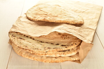 Several freshly baked pita bread in a paper bag, close-up, on a wooden table.