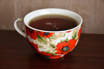Big red poppy cup of tea on the wooden table against the background of beige wallpaper.