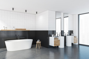 White and black bathroom with bathtub and two sinks near window