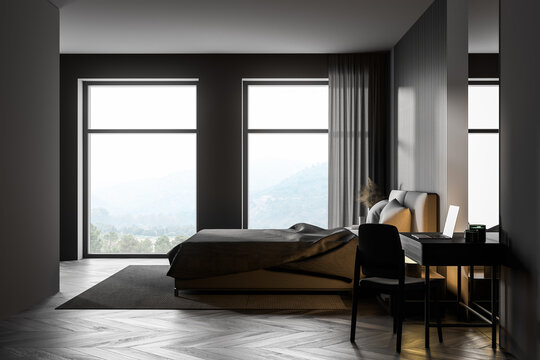 Dark bedroom interior with wooden floor, two large windows, a gray bed and two bedside tables. A cabinet with mirrors.