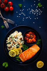 Fried salmon steak with risotto and  tomatoes roasted served on black plate on black wooden table
