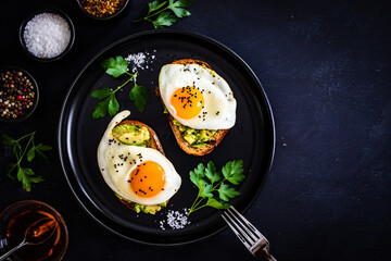 Continental breakfast - sunny side up eggs on toasted bread with avocado on black background

