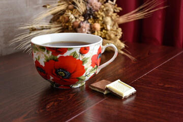 Poppy cup of tea and milk chocolate on the wooden table. 