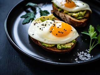 Continental breakfast - sunny side up eggs on toasted bread with avocado on black background
