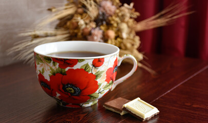 Big poppy cup of tea with sweets against the background of wild flowers.