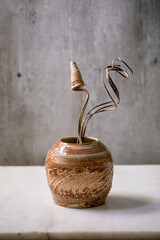 Dry flowers and twigs branch in brown ceramic vase on white marble table with gray wall behind....