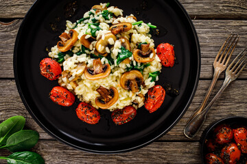 Risotto with champignon, roast tomatoes, spinach and parmesan on black table
