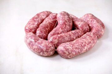 Bunch of Raw uncooked italian sausages salsiccia in plate on white marble background. Green salad, vegetables and tomato sauce around.