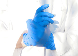 hands of doctor or nurse in protective medical gloves on white laboratory kittel background....