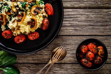 Risotto with champignon, roast tomatoes, spinach and parmesan on black table
