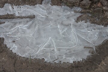 one large frozen puddle of white ice on the gray earth of the road