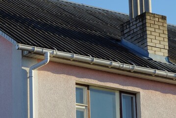 white plastic water pipe on brown wall of house with window under gray slate roof