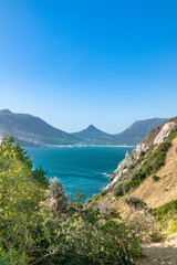 Fototapeta premium Meeresbucht mit Felsen und Büschen im Vordergrund im Hintergrund Häuser und Berge