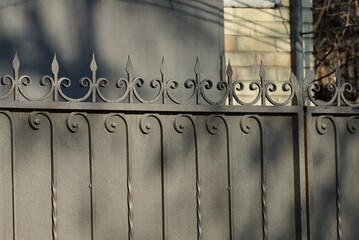 a fence made of black sharp iron forged pattern rods  on the wall in the street