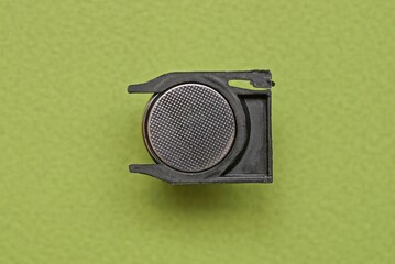 one gray metal round battery cell in a black plastic container on a green table