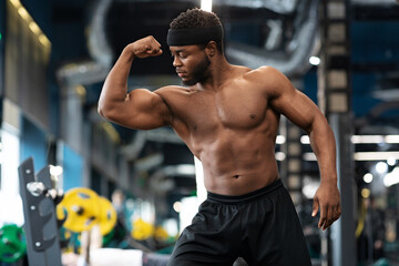 Fototapeta na wymiar Muscular black man playing with arm muscles in gym