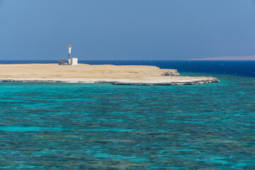 Lighthouse on sore with blue water and sand beach