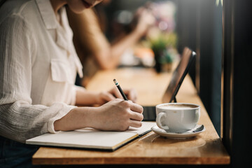 Close up of a woman hold a pencil taking notes and drinking coffee at the café.