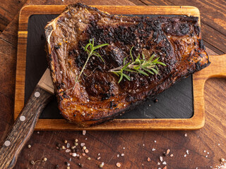 Grilled sashi beef bone steak with rosemary, black pepper, himalayan salt and a knife on a wooden board
