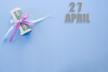 calendar date on blue background with rolled up dollar bills pinned by blue and pink ribbon with copy space. April 27 is the twenty-seventh day of the month