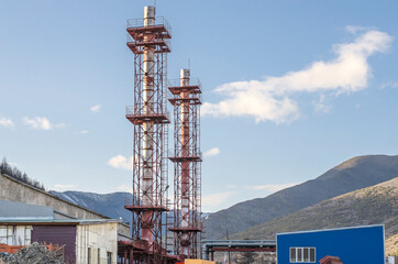 Pipes of a concrete plant against a blue sky in a mountainous area.