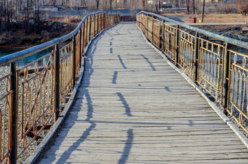 Wooden bridge with metal railing across the river close-up.