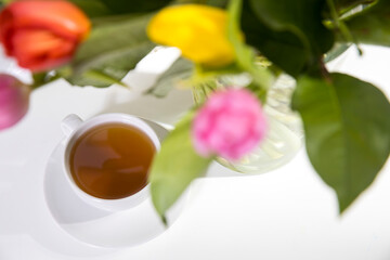 A bouquet of multi-colored tulips in a transparent vase and cup of tea