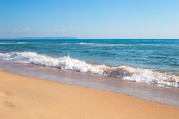 Fototapeta na wymiar Sea coast on a sunny day. Wave with foam on the sandy shore. Travel and tourism.