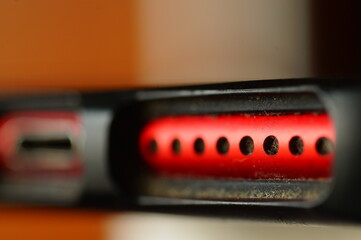 Cell phone - charging jack and speakers. Red, used phone in protective packaging. Electronics in close up.