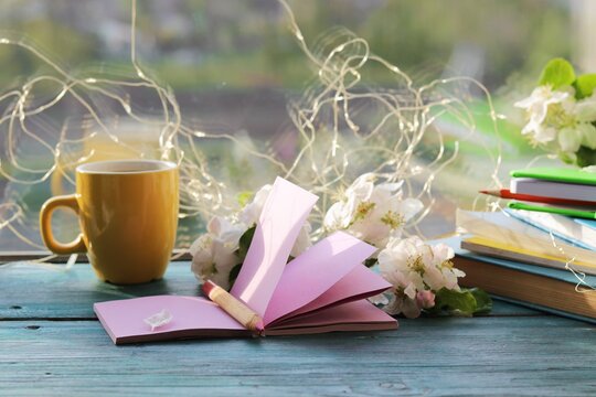 Cup of hot coffee, blank notebook, books, spring flowers on the windowsill, home learning concept, seasonal greetings