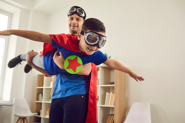 Dream big. Loving father helps his son fly like a superhero. Boy with pilot glasses play fly with his dad at home. Cheerful family in red cloaks and pilot glasses are having fun together.
