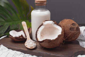 Glass bottle of milk or yogurt on dark wooden table with coconuts and coconut flakes