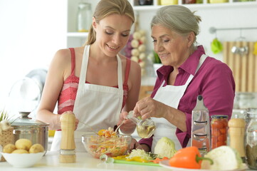 Smiling senior mother and adult daughter cooking together