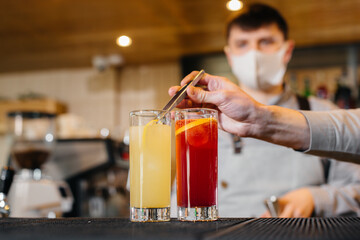 Two stylish bartenders in masks and uniforms during the pandemic, preparing cocktails. The work of restaurants and cafes during the pandemic.