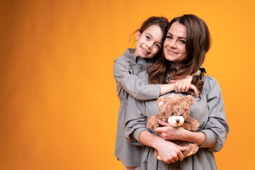 Mom holding a toy bear and daughter in pigtails hug and look at the camera. Family holiday
