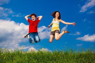 Girl and boy running, jumping against blue sky
