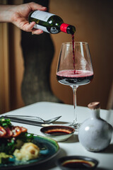 Selective focus shot of pouring red wine into the glass on a white table, dinner table at restaurant