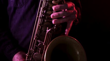 Close up of man playing vintage saxophone under red lights, handheld dolly in