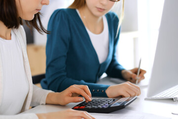 Accountant checking financial statement or counting by calculator income for tax form, hands close-up. Business woman sitting and working with colleague at the desk in office. Audit concept