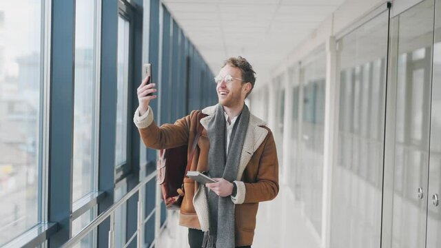 Cheerful charismatic man walking down the hall talking on video link