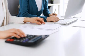 Accountant checking financial statement or counting by calculator income for tax form, hands close-up. Business woman sitting and working with colleague at the desk in office. Audit concept