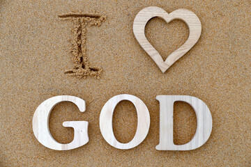 Wooden letters forming the word GOD  with heart on a background of beach sand. I love God. Christian symbol.  25.02.2017