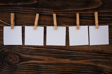 Clothespins with blank sheets of paper hanging on a wooden background. Background for your inscriptions.