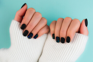 Young Woman's hands in white knitted sweater on blue background. Perfect black matte manicure with...