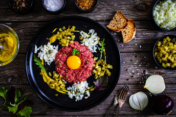Beef tartare steak with onion, capers and pickled cucumbers on wooden table