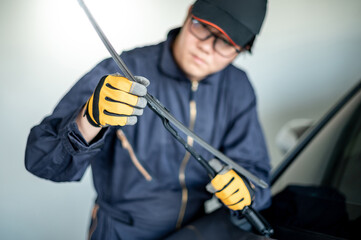Young Asian auto mechanic checking windshield wiper in auto service garage. Mechanical maintenance engineer working in automotive industry. Automobile servicing and repair