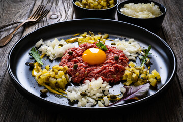 Beef tartare steak with onion, capers and pickled cucumbers on wooden table