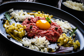 Beef tartare steak with onion, capers and pickled cucumbers on wooden table