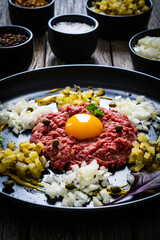 Beef tartare steak with onion, capers and pickled cucumbers on wooden table